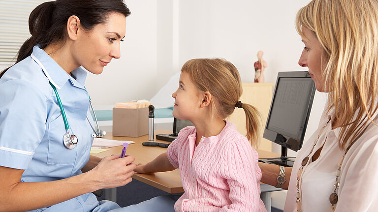 A nurse tending to a child patient, who is sitting on her mothers lap.
