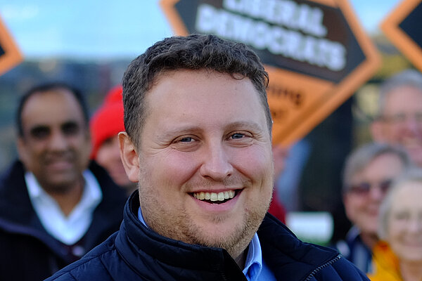 Dr Will Sapwell in front of a Lib Dem poster